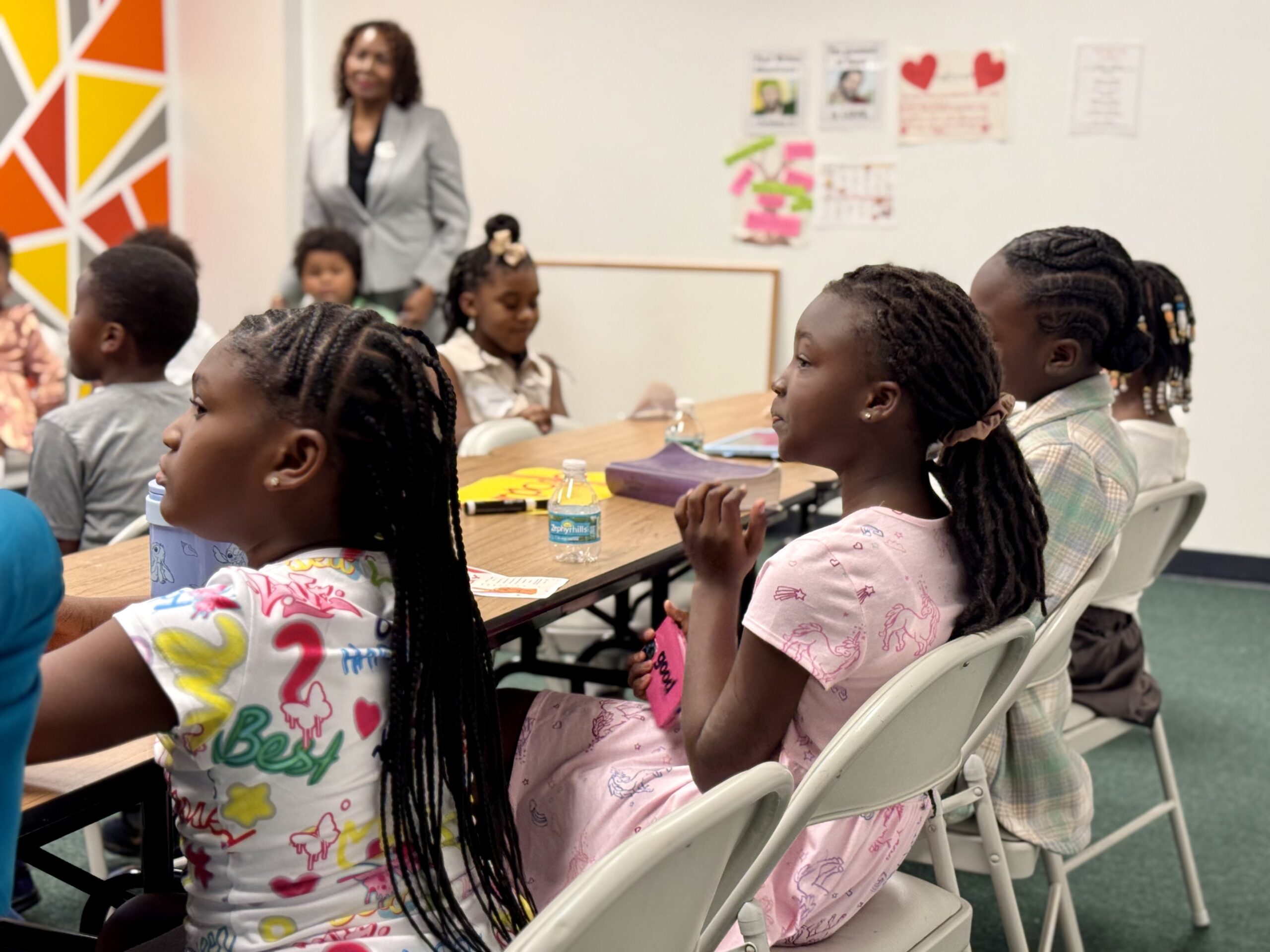 Children seated at a table with Bibles, listening to a speaker during Bible study