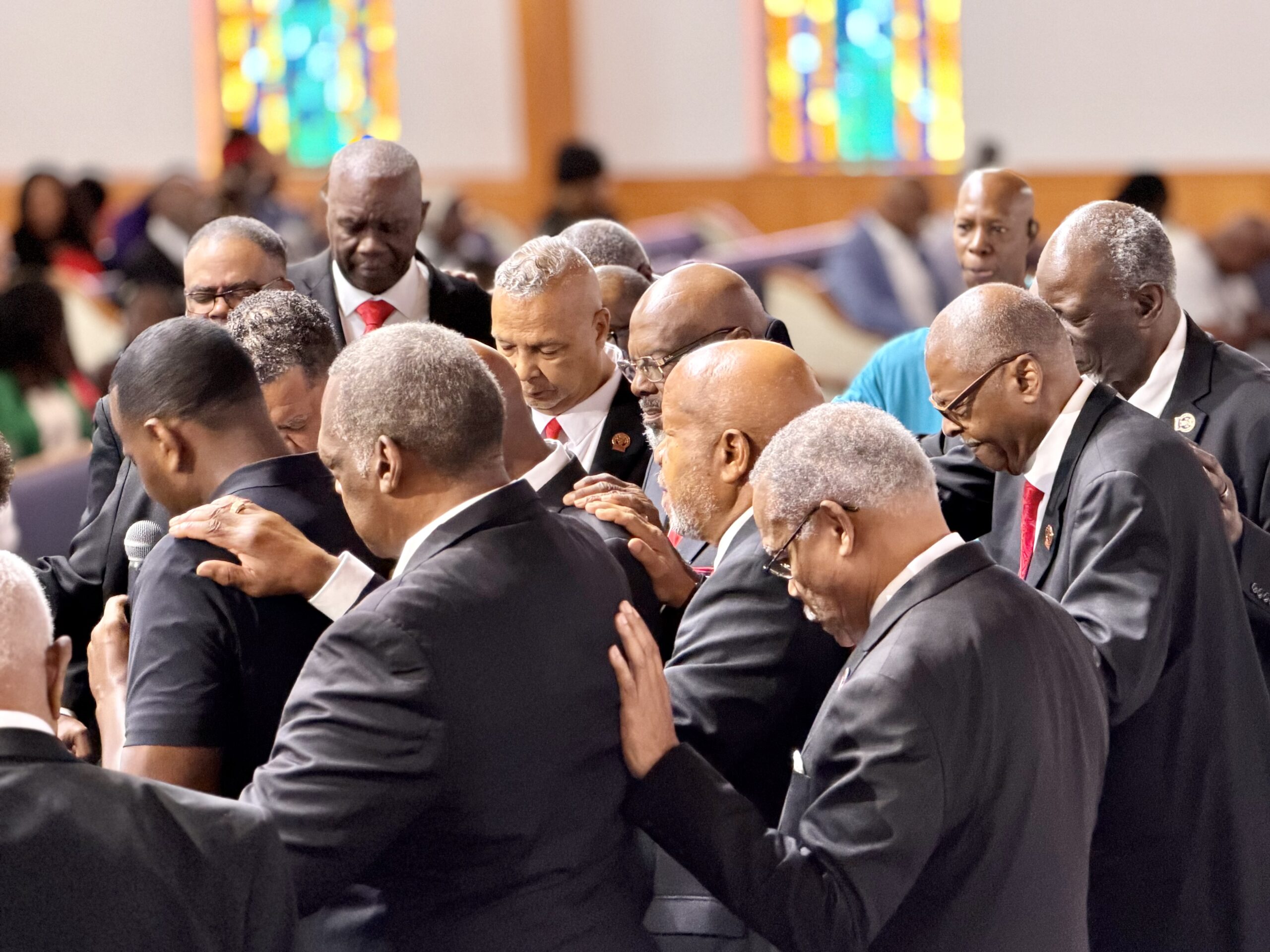 Men of the church gathered in prayer with heads bowed, praying over someone
